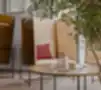 Moderna biroja kafijas zona ar Boxy akustiskajiem atpūtas krēsliem, koka paneļiem, zaļajiem augiem un apaļu kafijas galdiņu.