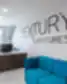 Modernus „Nextury Ventures“ registratūros interjeras su mediniu lenktu stalu, mėlyna sofa ir logotipu ant baltos sienos.